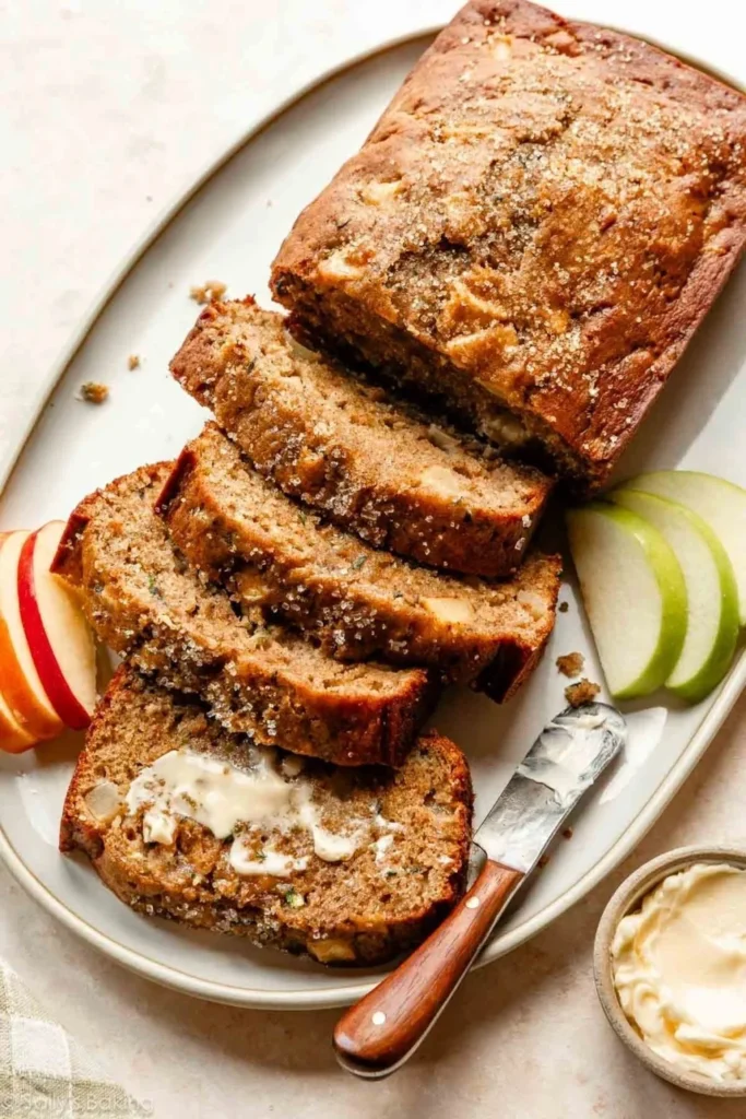 Sliced Apple Zucchini Bread on a wooden board with apples nearby